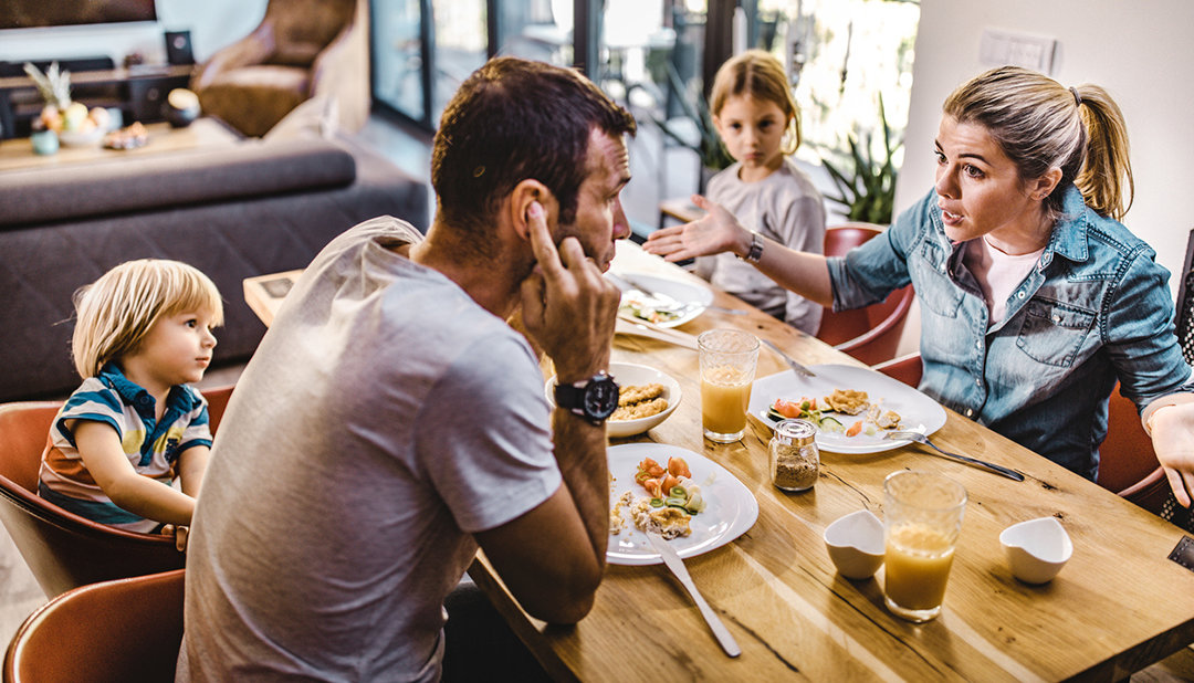 Family at a dinner with the husband with his hands over his ears