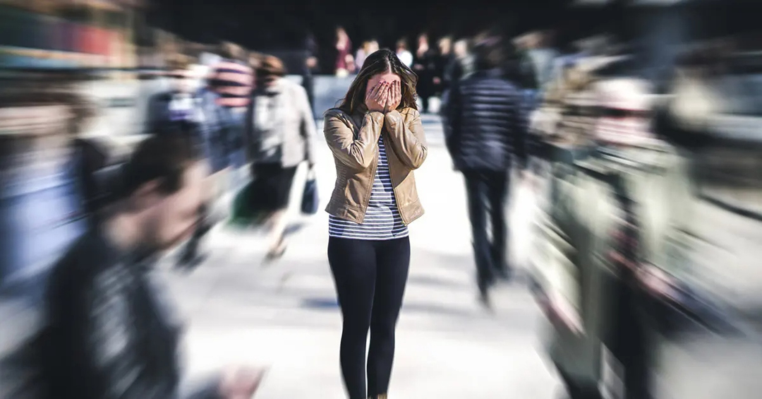 Woman in a crowd with her hands covering her face, crowd around her is blurred out