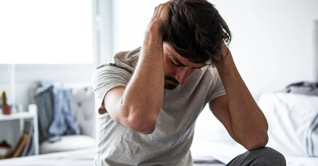 Man sitting on his bed, rubbing the back of his head