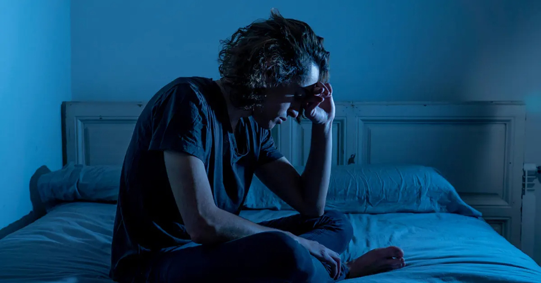 A man sitting cross-legged on his bed, at night
