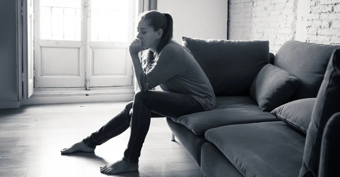 Woman sitting in a living room on a couch, the image is monochromatic