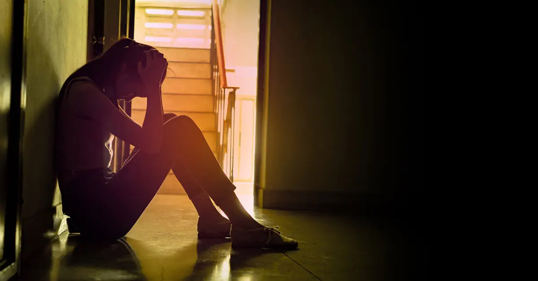 Woman sitting on the floor next to a stairwell with her head in her hands