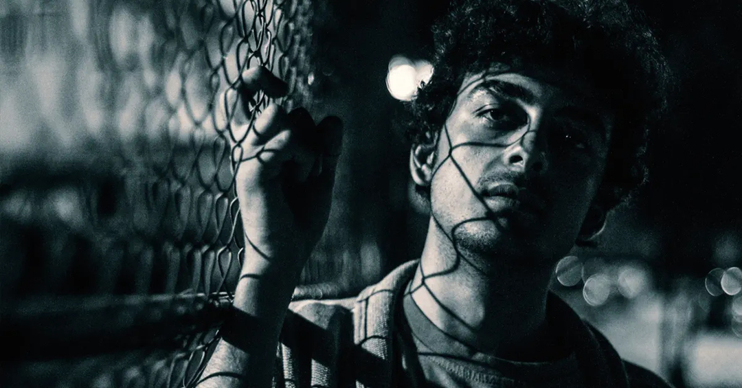 A monochromatic image of a man standing next to fence