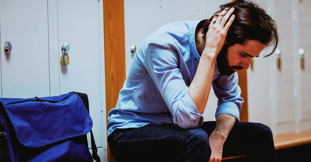 Man in front of lockers holding his head