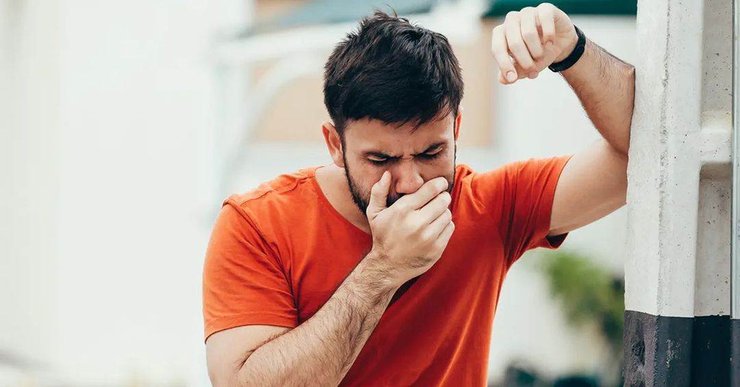 Man on the street leaning against a structure who is suffering from nausea