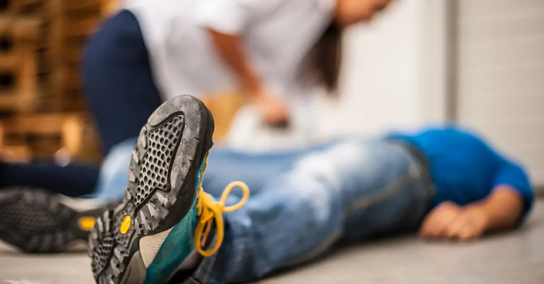 Man on his back on the floor, woman kneeling over him checking for his state