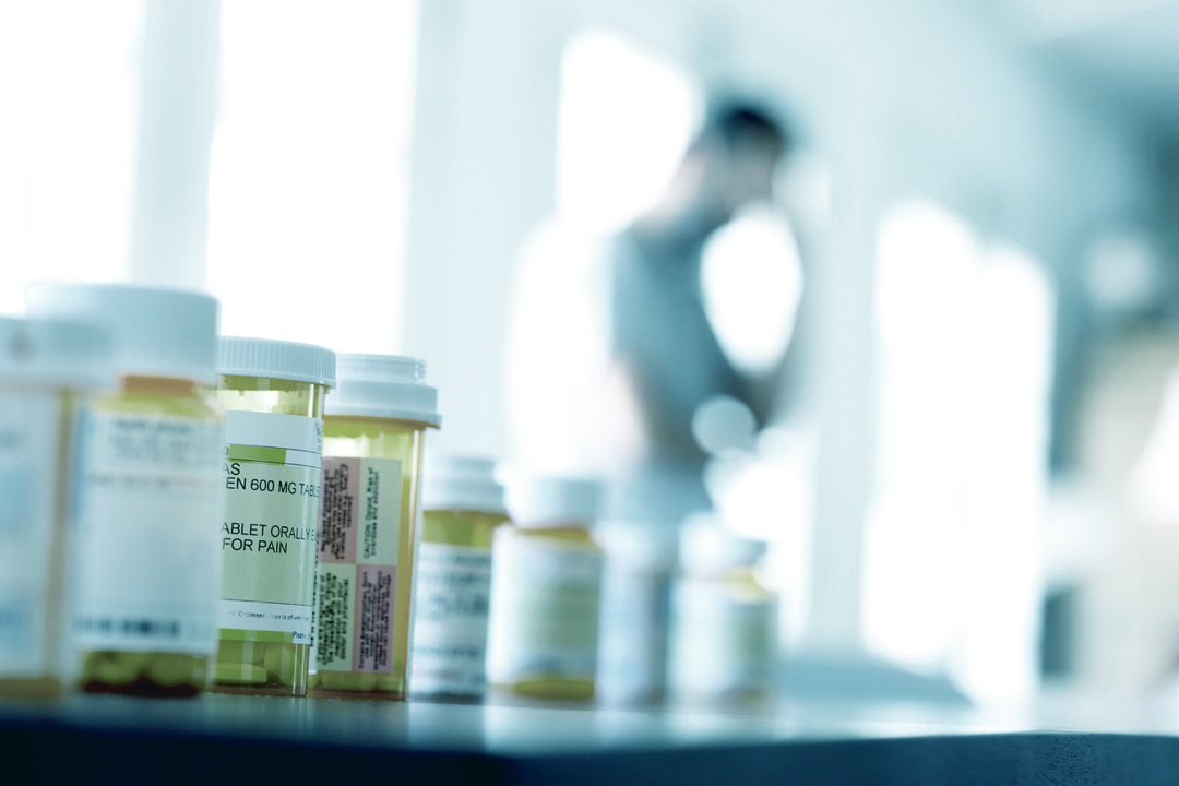 Table with prescription drug bottles. Silhouette of a man in distance.