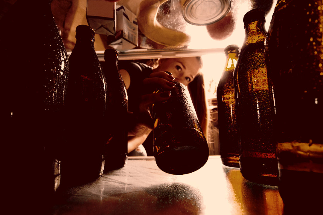 Woman takes beer from fridge