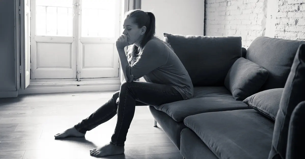 Woman sitting in a living room on a couch, the image is monochromatic
