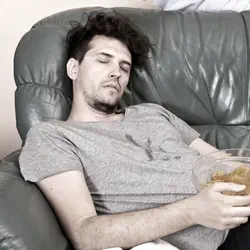 Man sitting on his couch which is somewhat messy