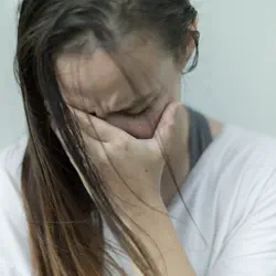A woman in a white shirt holding her head in pain