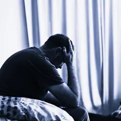 Man sitting in a dark room with his hand on his head