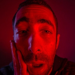 Man's face, in red light, looks like on a drug trip