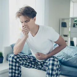 A man sitting on his bed with stomach pain and nausea
