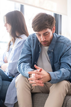 Wife and Husband seated next to each other, looking away from each other in sullen silence