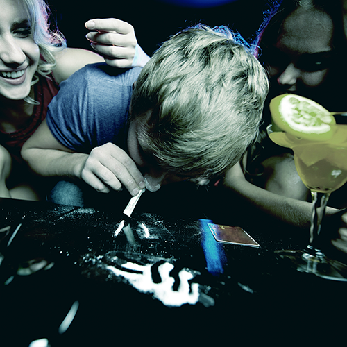A Man snorting Cocaine in a Club setting while seated at a table