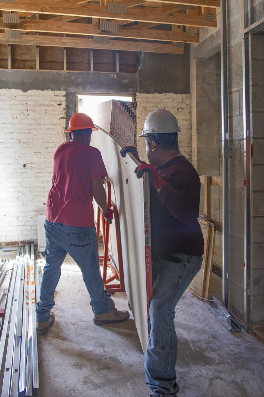 Workers receive drywall through window.