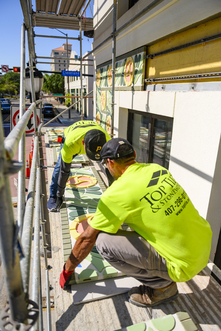 Tile specialists prepare to position handcrafted terracotta pieces along the façade.