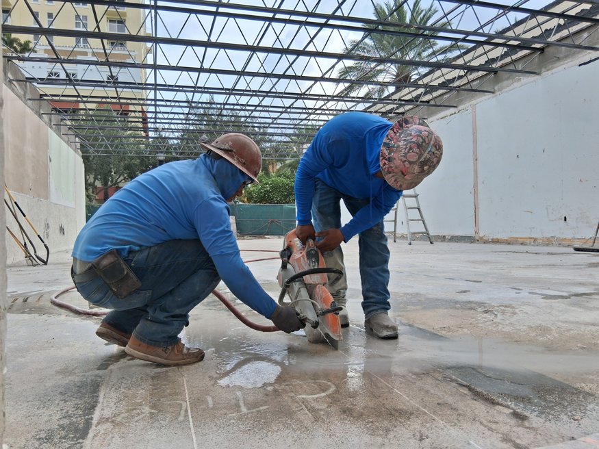 Workers cut concrete along planned utility trench.