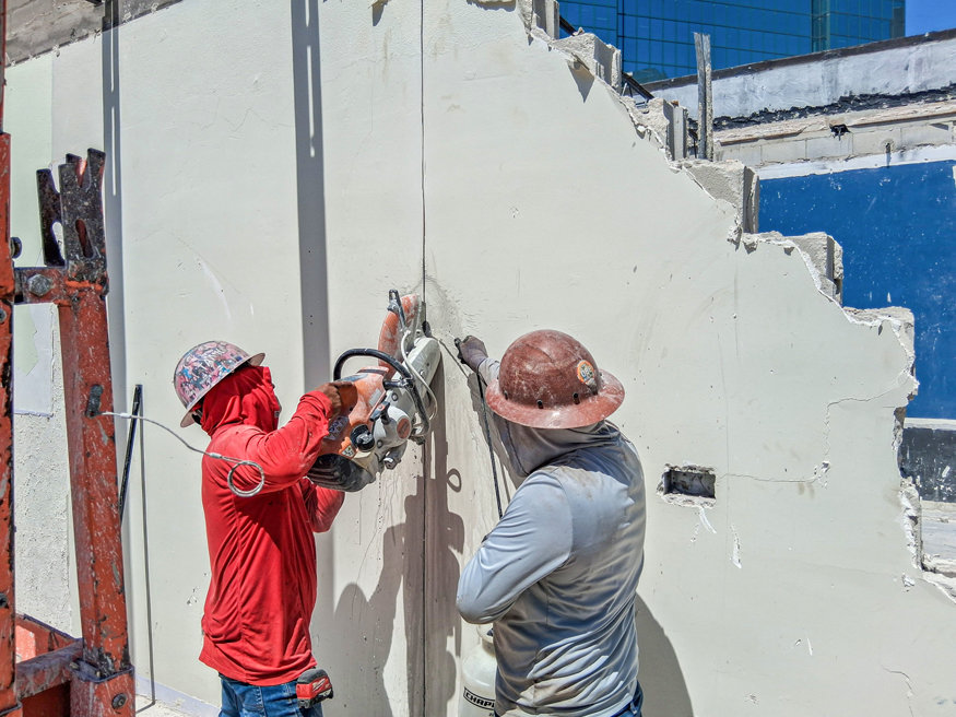 Workers cut concrete wall with saw.