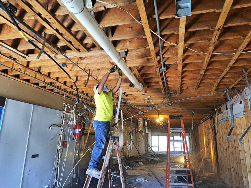 Renovation work underway at 623 Cleveland Street, with a crew member installing overhead piping as part of the interior rebuild.