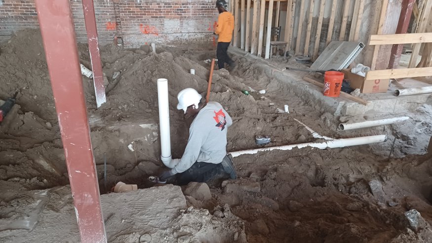 Workers aligning and securing hard plastic pipes in a freshly excavated interior trench.