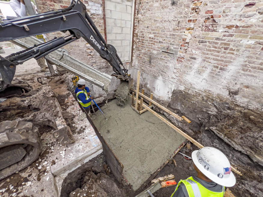Construction workers use an excavator chute to pour concrete into a framed elevator shaft pit at the Woolworth building.