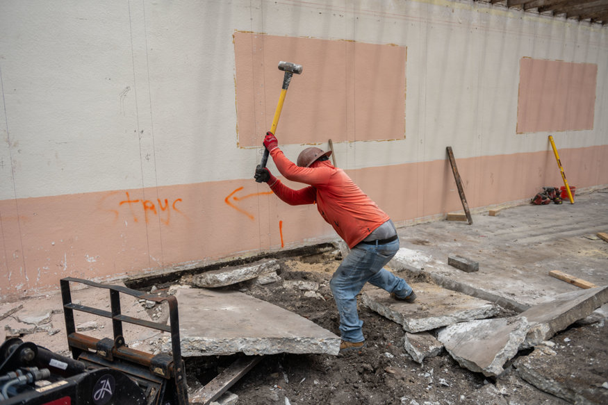 Crew member breaks a saw-cut concrete slab section with a sledgehammer.