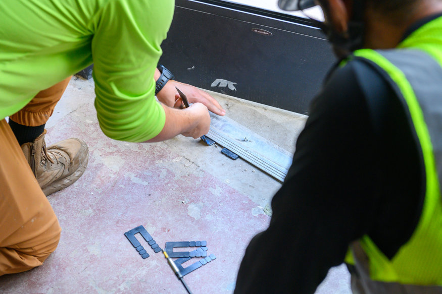 Workers adjusting metal threshold at storefront base.