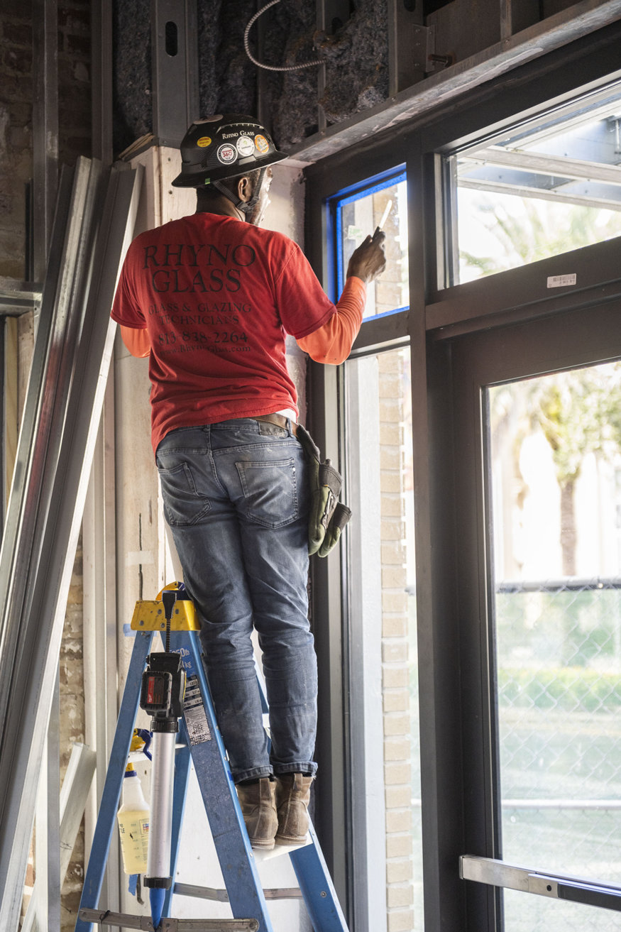 Worker sealing edges of storefront glass.
