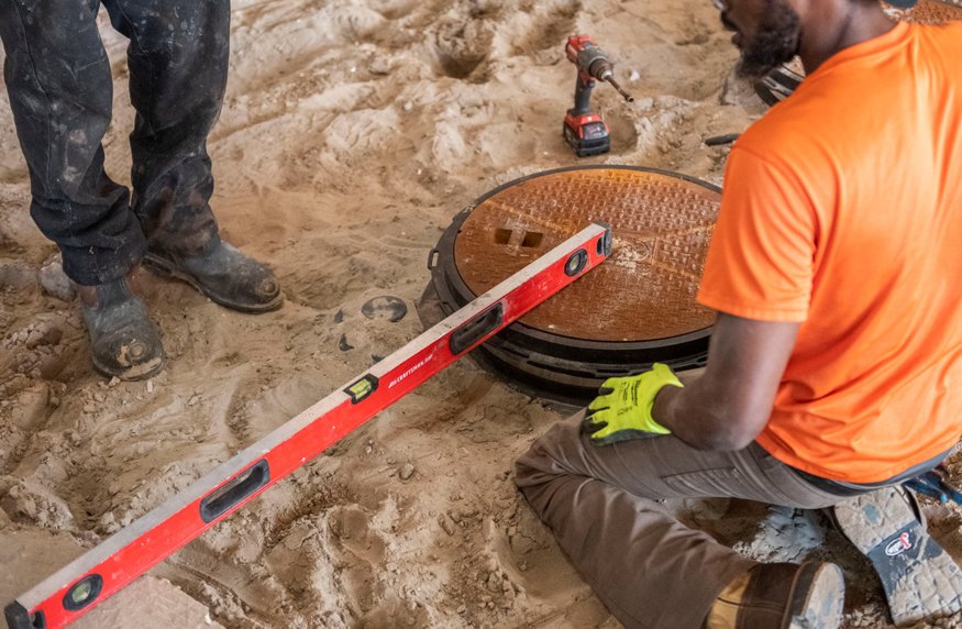 Worker uses a level to align grease trap lid with concrete slab grade at Peoples Bank.