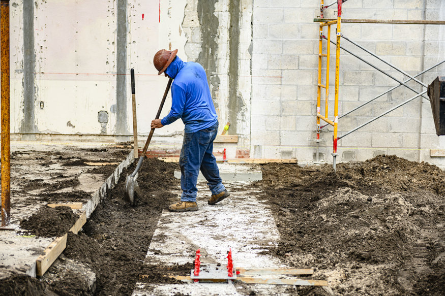 Worker spreads soil around completed concrete footing.
