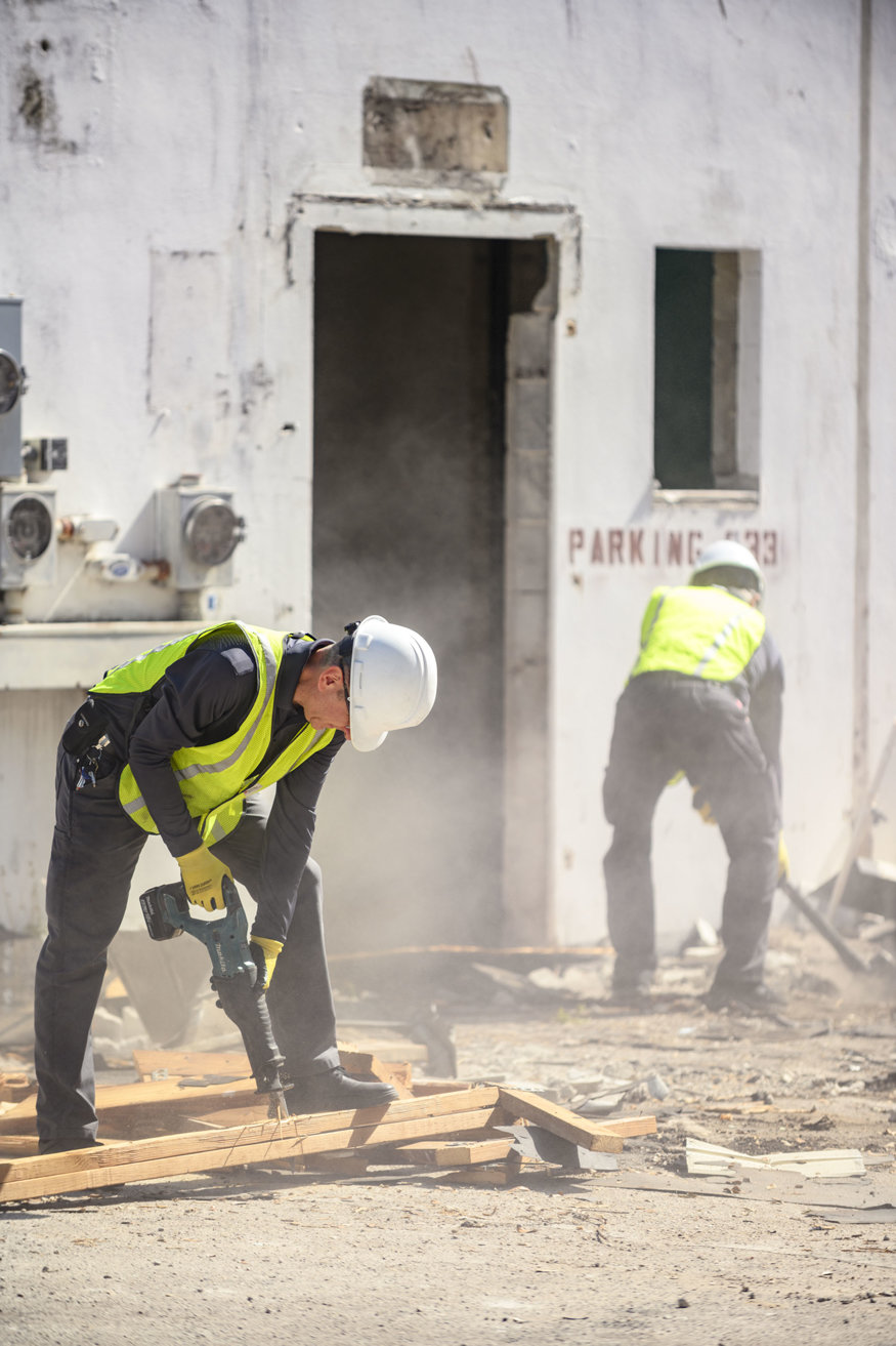 Workers using jackhammer to dismantle wood framing. 
