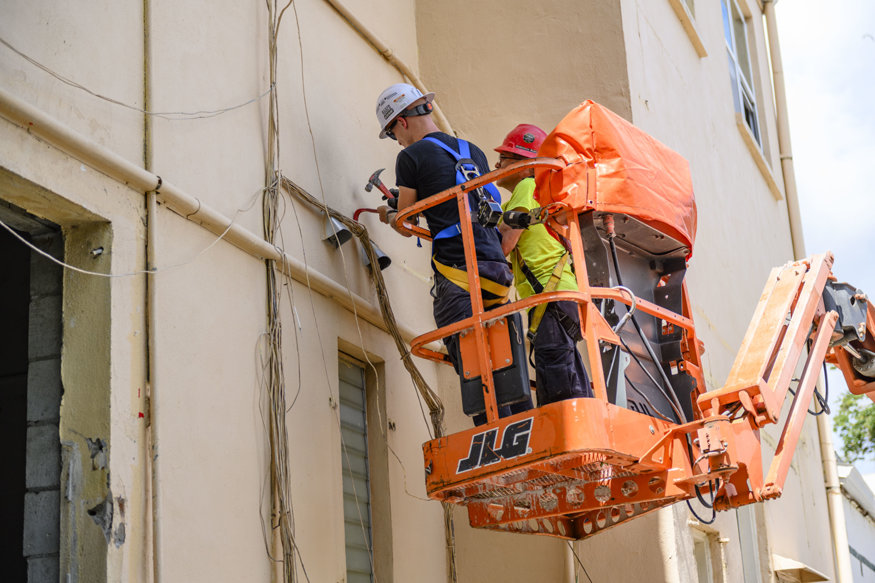 Workers remove exterior wiring from Brown Brothers using an aerial lift.