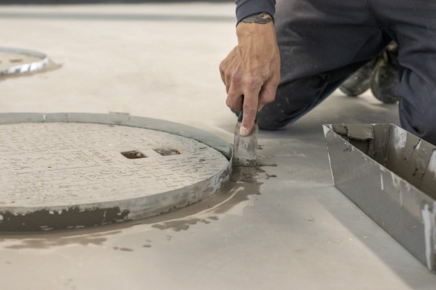 Concrete being finished around raised grease trap lid.