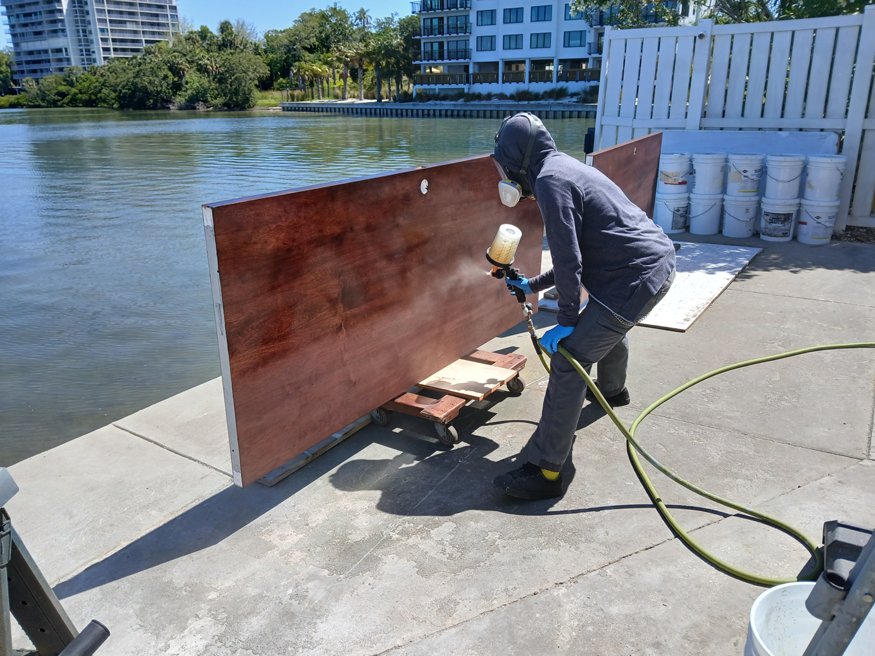 Worker spraying clear coat on a stained birch door to protect and complete the restoration process at the Telephone Building.