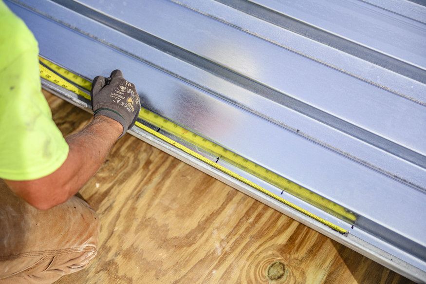 Worker marks corrugated metal decking panel for installation.