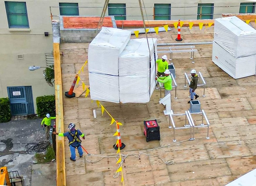 Workers guiding a roofing pallet onto the roof.