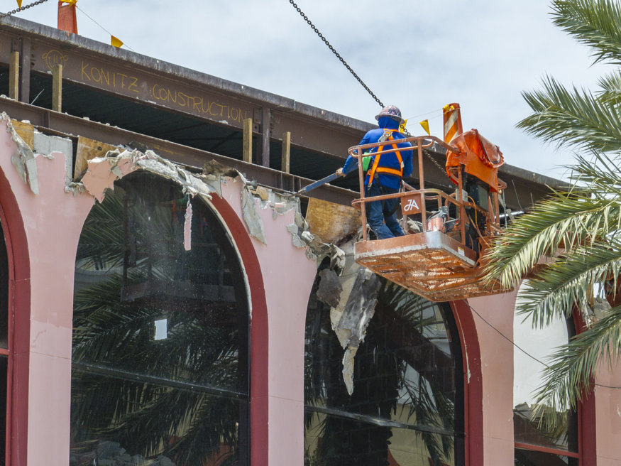 Worker removes façade material from building.