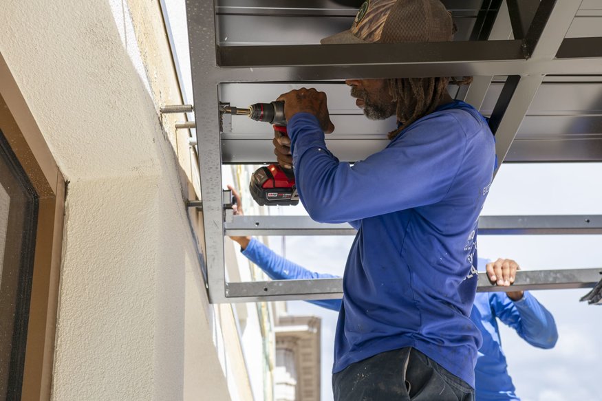 Worker fastening steel awning frame with drill. 