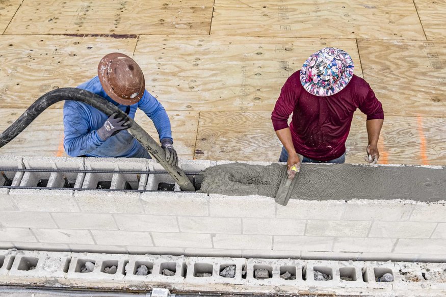Workers place and smooth concrete within reinforced parapet masonry.