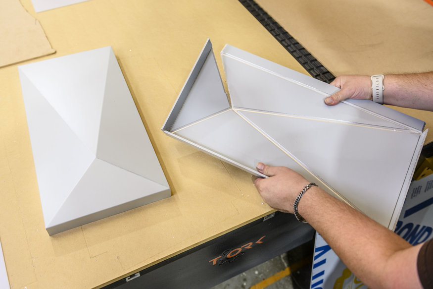 Worker inspecting folded aluminum façade prototype panel.