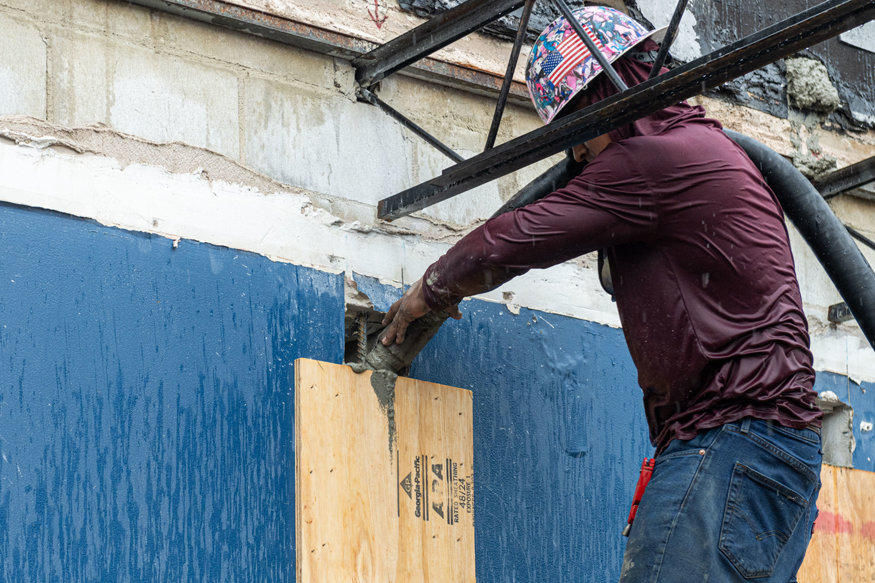 Worker guides concrete hose into an open CMU wall cell.