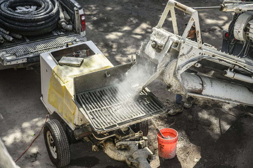 Cementitious grout flows from equipment for CMU wall filling.