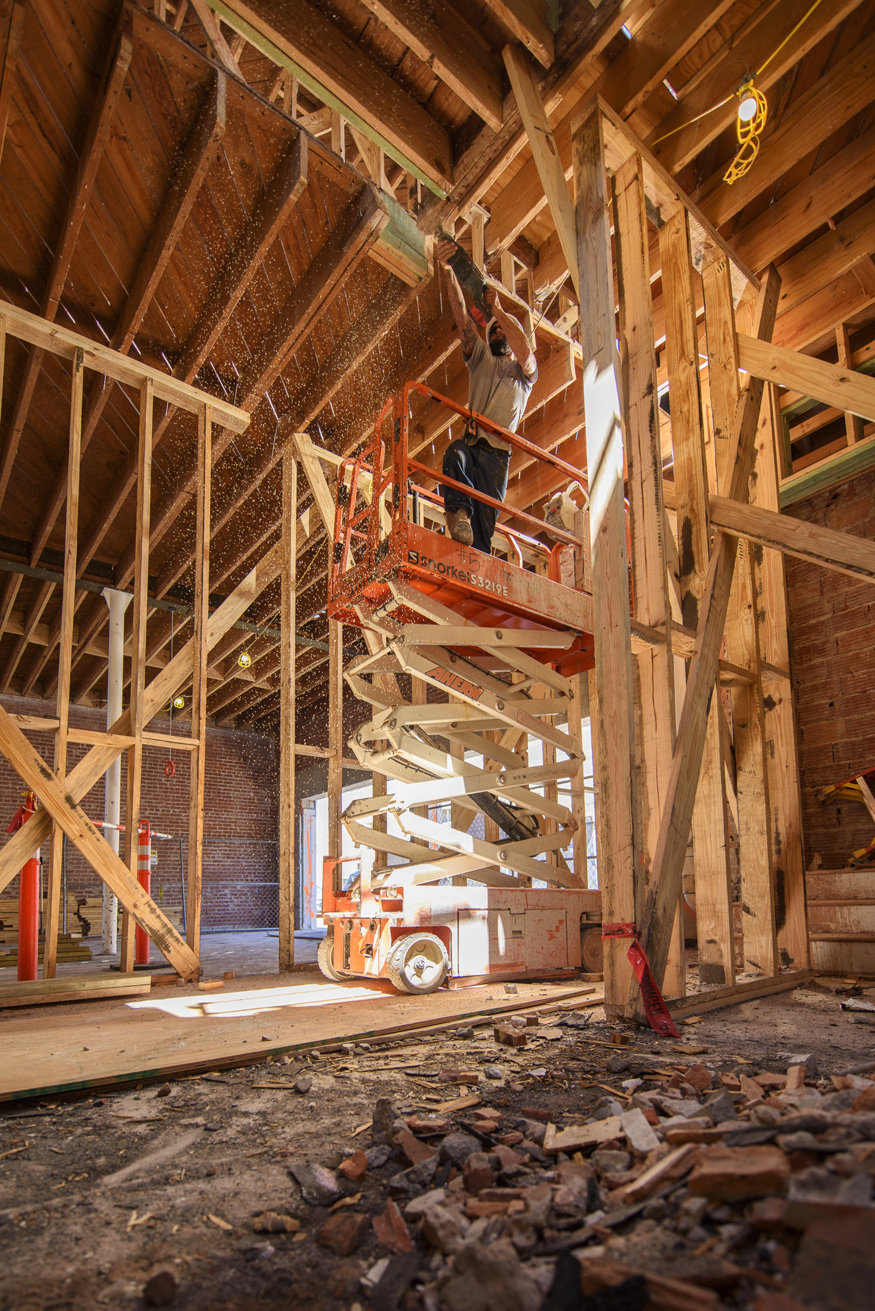 Construction worker on a scissor lift performing structural work on the second floor of the Peoples Bank building.