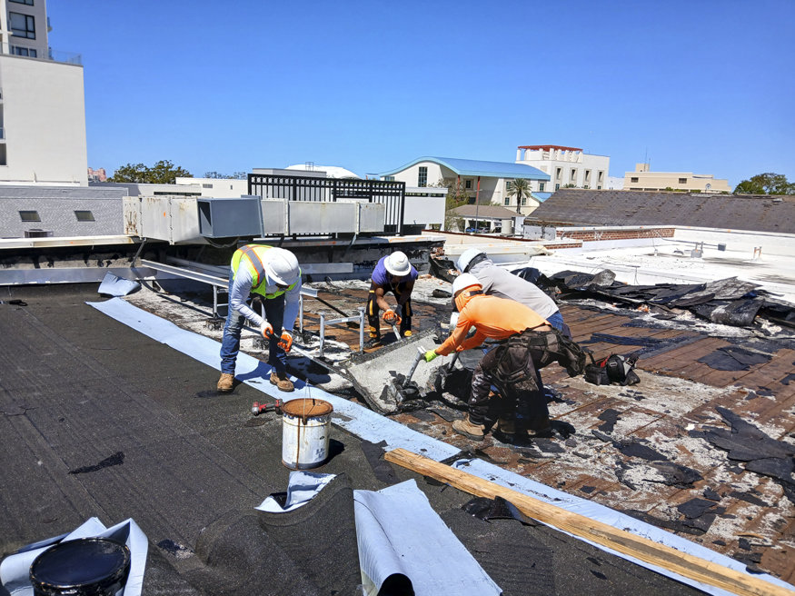 A crew works on removing the roof and installing temporary weatherproofing to protect the Peoples Bank building during renovations.