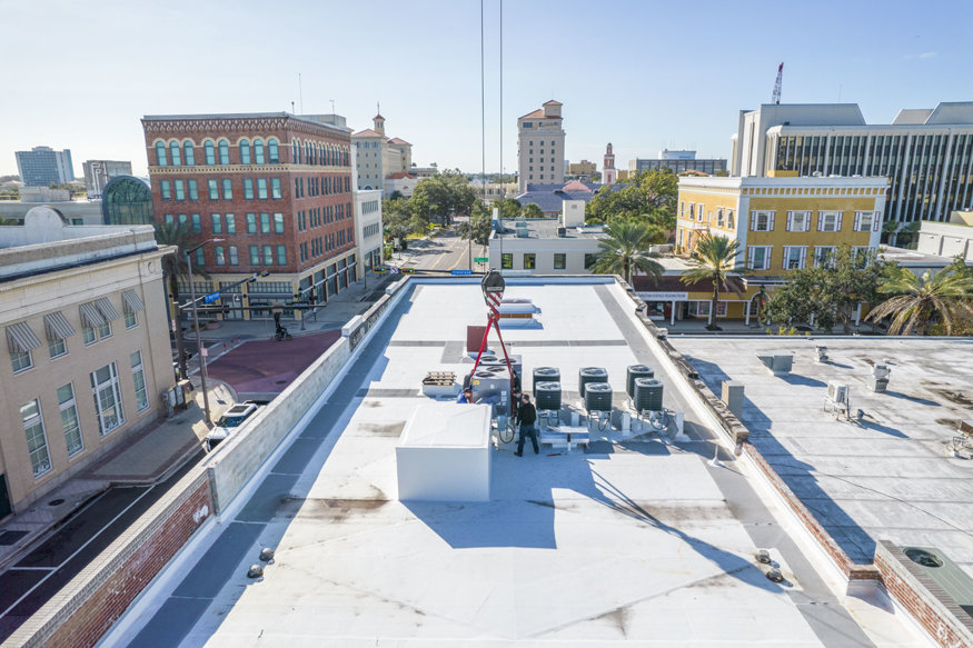 Workers guiding rooftop unit.