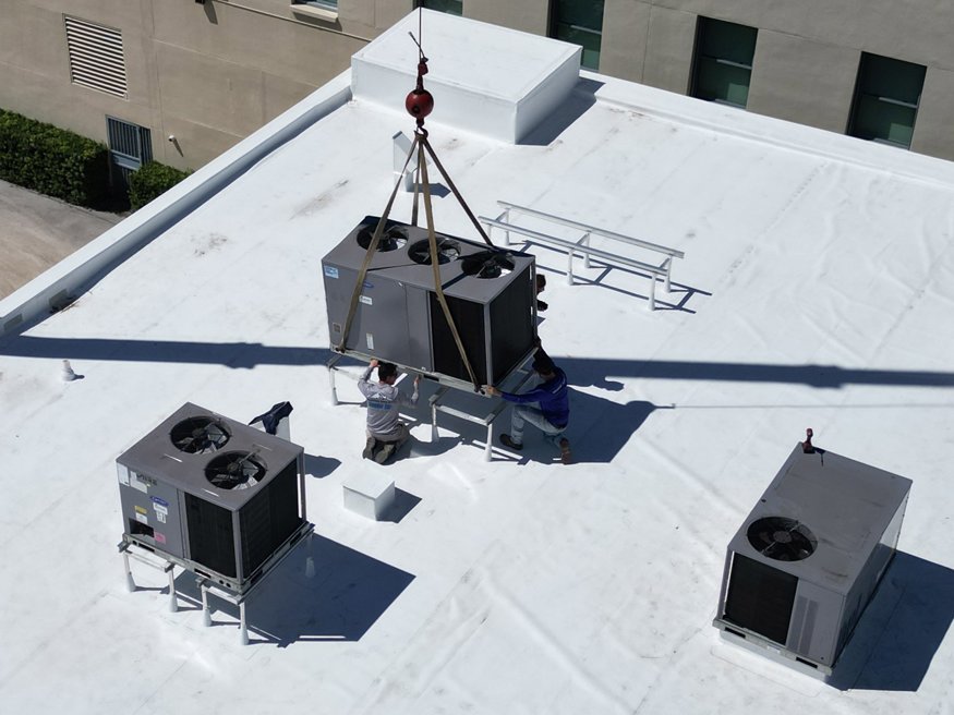 HVAC crew guiding AC unit into place on the roof.
