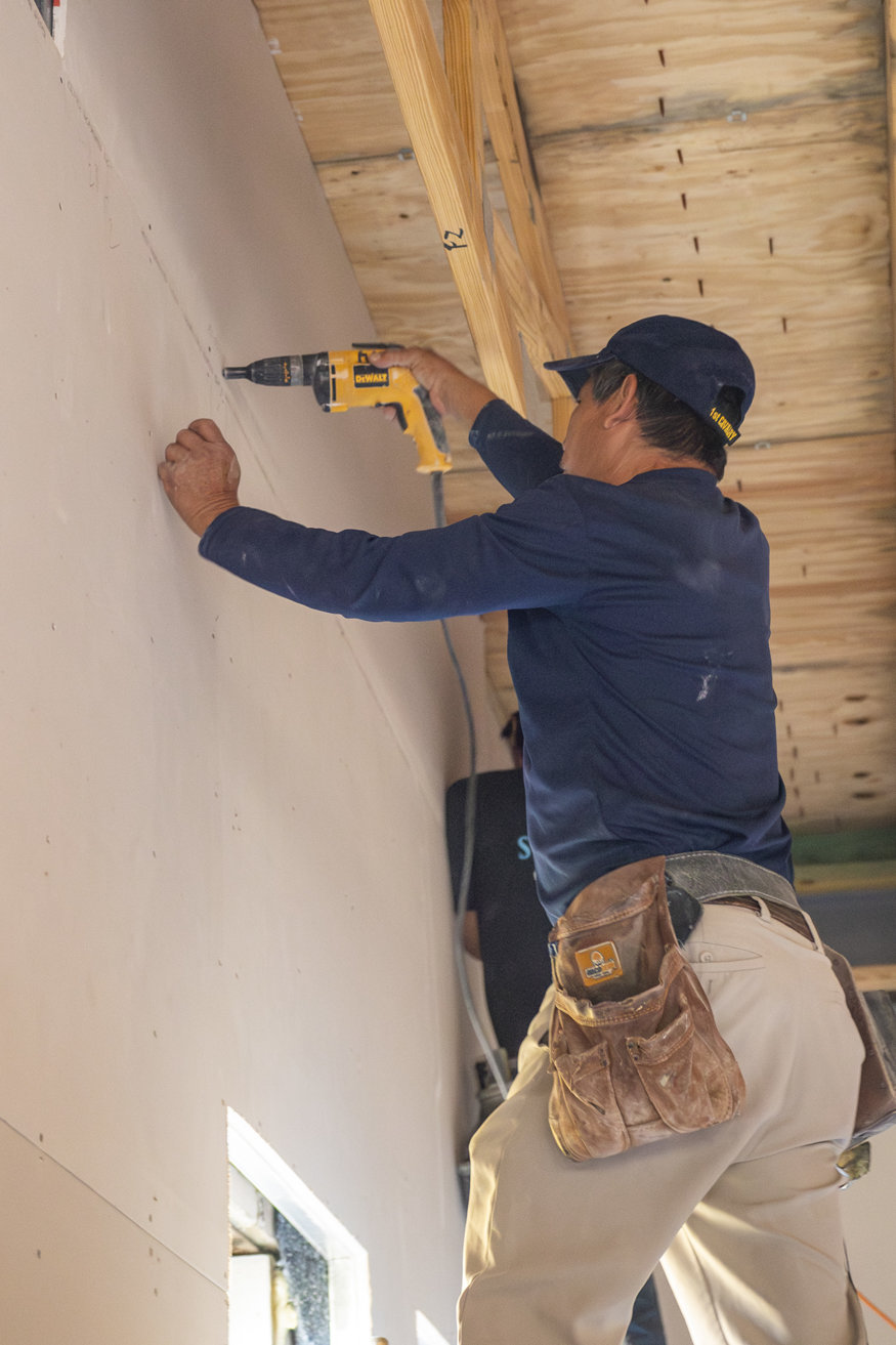 Worker fastening drywall panels to framing.