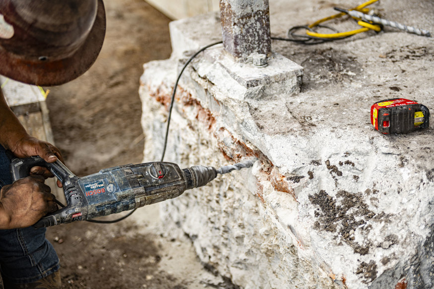Rotary hammer drills into existing concrete footing.
